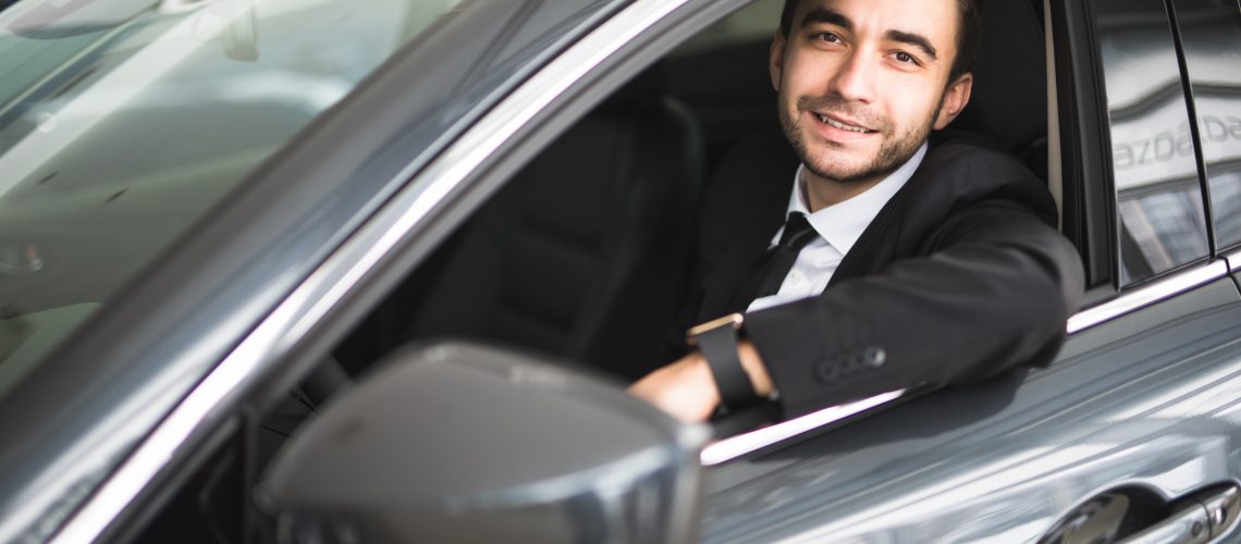 happy smiling driver in the car, portrait of young successful business man over window of car